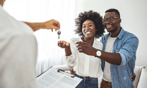 Handsome realtor is giving key to the new apartment to happy young couple. Couple buying new apartment.  A young couple receive the keys to their new apartment from a letting agent.